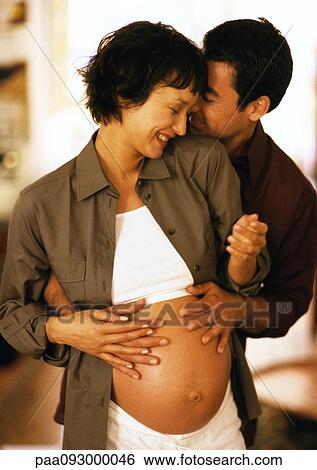 Stock Photograph - Man touching pregnant woman's stomach from behind. Fotosearch
