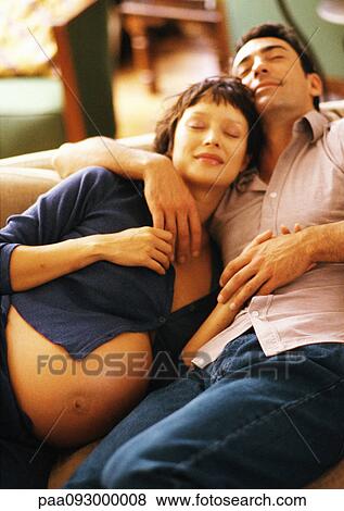 Stock Photo - Pregnant woman and man lying on sofa, smiling. Fotosearch