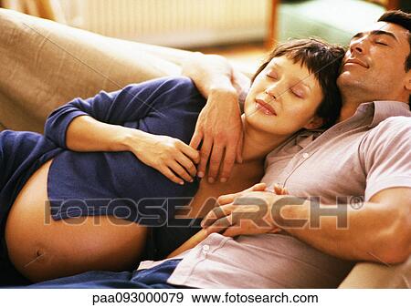 Stock Photo - Pregnant woman leaning head on man's chest, on sofa. Fotosearch