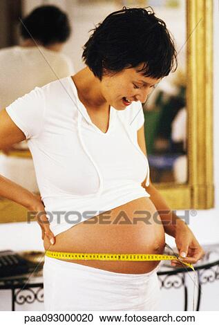 Stock Image - Pregnant woman measuring her stomach. Fotosearch