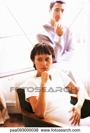 Stock Photo - Pregnant woman sitting in armchair, man in background. Fotosearch