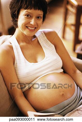 Stock Image - Pregnant woman sitting in armchair, smiling at camera, portrait. Fotosearch