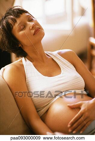Stock Photo - Pregnant woman sitting in armchair, eyes closed and hand on belly. Fotosearch