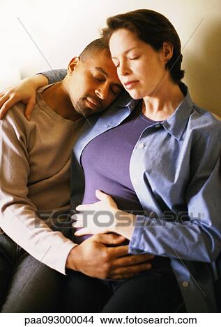 Picture - Pregnant woman sitting with arm around man, portrait. Fotosearch