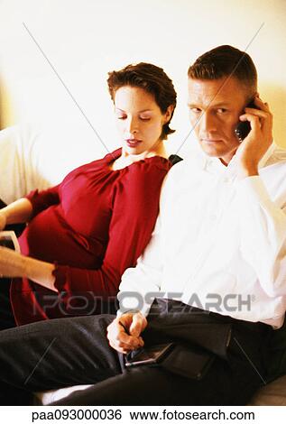 Stock Photograph - Pregnant woman sitting with man using cell phone. Fotosearch