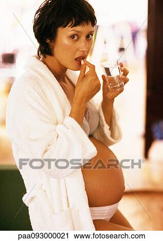 Stock Image - Pregnant woman taking a pill, portrait. Fotosearch