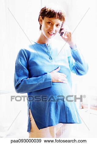 Stock Photo - Pregnant woman using cell phone, smiling at camera, portrait. Fotosearch
