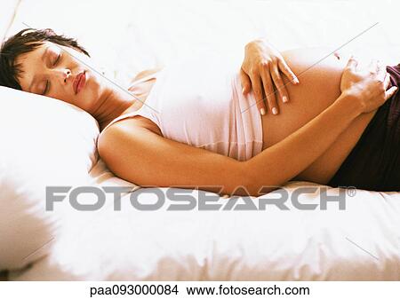 Picture - Pregnant woman with eyes closed, lying on back on bed. Fotosearch