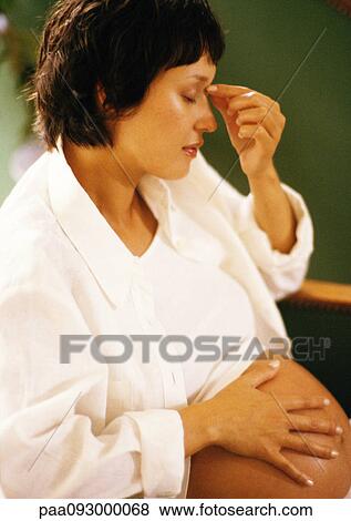 Stock Photo - Pregnant woman with hand on stomach, touching bridge of nose. Fotosearch
