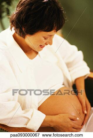 Stock Photo - Pregnant woman with hands on stomach, looking down. Fotosearch