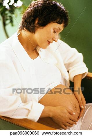 Stock Photograph - Pregnant woman with hands on stomach, looking down. Fotosearch