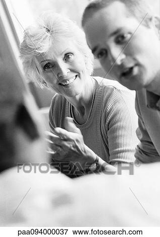 Stock Photo - Businessman and woman looking at colleague, blurred foreground, B&W. Fotosearch