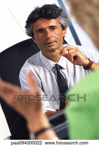 Stock Image - Businessman at desk, listening to woman in blurred foreground . Fotosearch