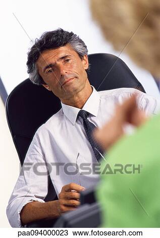 Businessman at desk, listening to woman in blurred foreground View Large Photo Image Stock Image - Businessman at desk, listening to woman in blurred foreground . Fotosearch