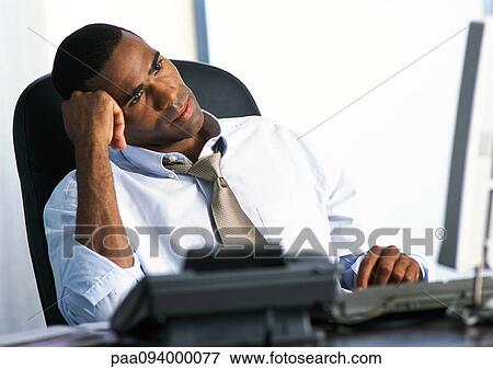 Businessman sitting at desk, head leaning on hand View Large Photo Image Stock Photo - Businessman sitting at desk, head leaning on hand. Fotosearch