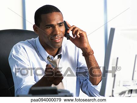 Stock Photo - Businessman sitting at desk, using telephone . Fotosearch