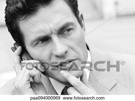 Businessman using cell phone with finger on chin, close-up, B&W View Large Photo Image Stock Photo - Businessman using cell phone with finger on chin, close-up, B&W. Fotosearch