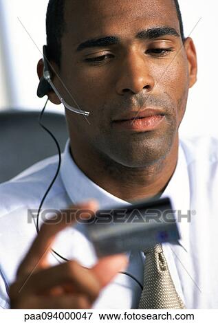 Businessman wearing headset, looking down at credit card in hand, close-up View Large Photo Image Stock Photo - Businessman wearing headset, looking down at credit card in hand, close-up. Fotosearch