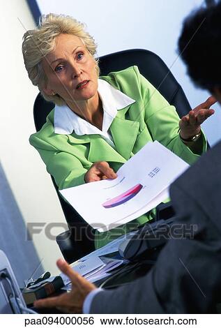 Stock Photograph - Businesswoman handing document to colleague, blurred foreground. Fotosearch