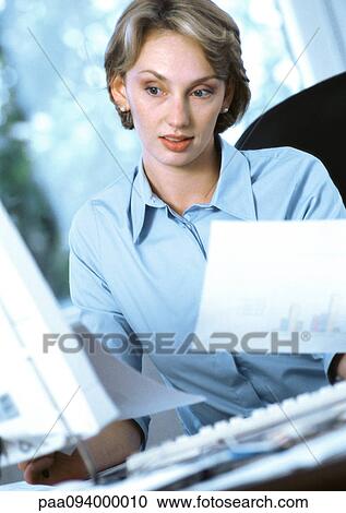 Stock Image - Businesswoman holding documents, looking at computer. Fotosearch