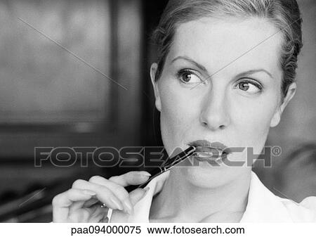 Stock Photography - Businesswoman holding pen at corner of mouth, close-up, B&W. Fotosearch
