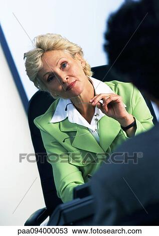 Businesswoman sitting in armchair looking at person in blurred foreground View Large Photo Image Stock Image - Businesswoman sitting in armchair looking at person in blurred foreground. Fotosearch