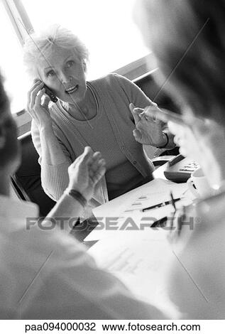 Mature businesswoman in conference, using cell phone, other businesspeople blurred in foreground, B&W View Large Photo Image Stock Image - Mature businesswoman in conference, using cell phone, other businesspeople blurred in foreground, B&W. Fotosearch