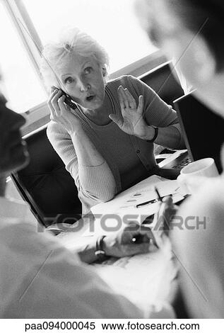 Mature businesswoman using cell phone, colleagues in blurred foreground, B&W View Large Photo Image Stock Photography - Mature businesswoman using cell phone, colleagues in blurred foreground, B&W. Fotosearch