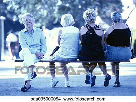 Picture - Four women sitting on a bench, three seen from the back. Fotosearch