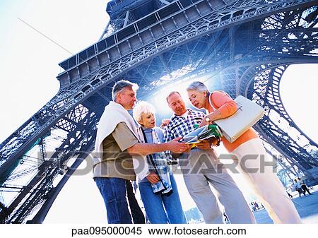 Stock Photography - France, Paris, group of mature tourists examining a map in front of Eiffel Tower, low angle view. Fotosearch