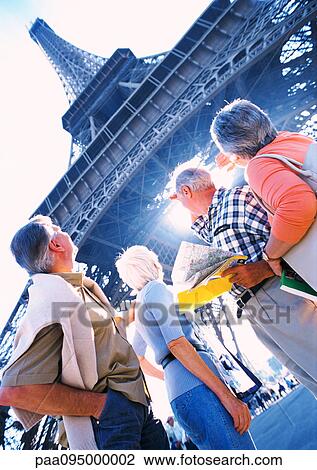Stock Image - France, Paris, mature tourists looking up at Eiffel Tower, view from below. Fotosearch