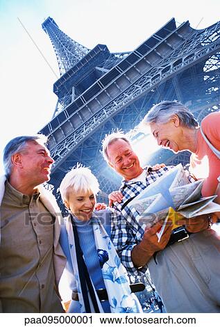 Stock Image - France, Paris, mature tourists examining a map in front of Eiffel Tower, view from below. Fotosearch