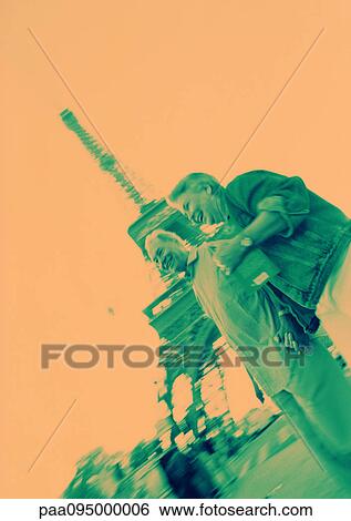 Stock Photograph - France, Paris, mature woman and man in front of Eiffel Tower, orange and green tones. Fotosearch