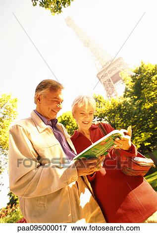 Stock Photo - France, Paris, mature woman and man examining a book, Eiffel Tower in background. Fotosearch