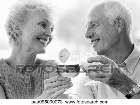 Stock Image - Mature man and woman clinking glasses, close-up, B&W. Fotosearch