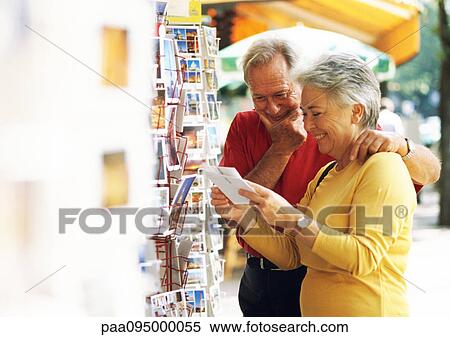 Stock Photography - Mature man and woman looking at postcards in the street. Fotosearch
