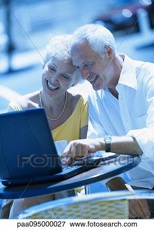 Stock Photo - Mature woman and man sitting at a cafe terrasse with laptop computer. Fotosearch