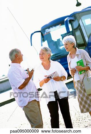 Stock Photo - Mature women and man talking in front of a tour bus. Fotosearch