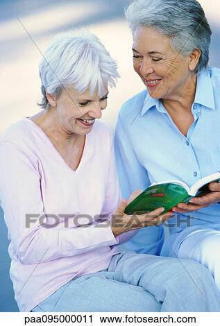 Two mature women sitting side by side, holding a book View Large Photo Image Stock Image - Two mature women sitting side by side, holding a book. Fotosearch