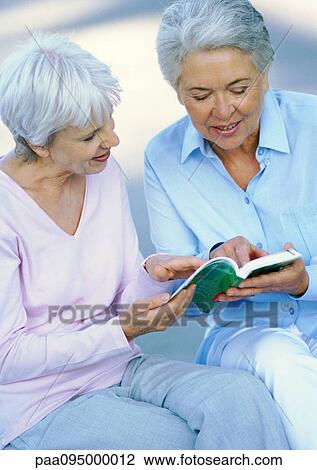 Two mature women sitting side by side, examining a book View Large Photo Image Stock Image - Two mature women sitting side by side, examining a book. Fotosearch