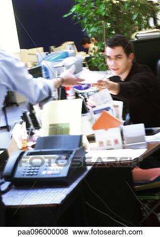 Stock Photo - In office, man handing document to second person, blurred. Fotosearch