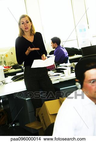 In office, woman standing with document, gesturing, other people working View Large Photo Image Picture - In office, woman standing with document, gesturing, other people working. Fotosearch