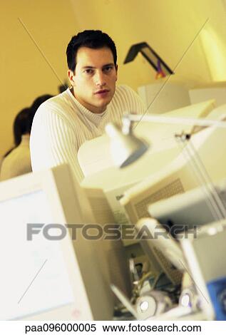 Stock Photography - Man behind computers in office, portrait. Fotosearch