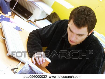 Stock Image - Man looking down, having a coffee at desk. Fotosearch
