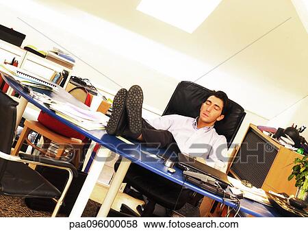 Stock Photo - Man sitting with feet on desk, eyes closed. Fotosearch