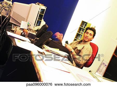 Stock Photograph - Man sitting with feet on desk, looking at camera. Fotosearch