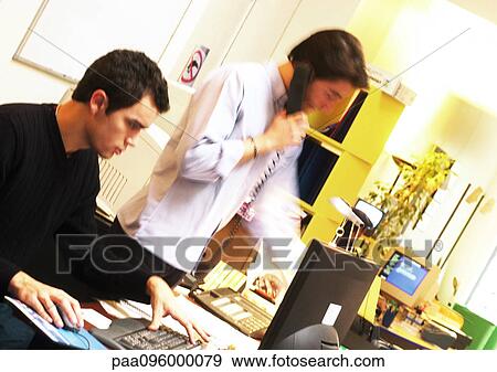 Man working on computer and man standing with telephone View Large Photo Image Stock Photo - Man working on computer and man standing with telephone. Fotosearch