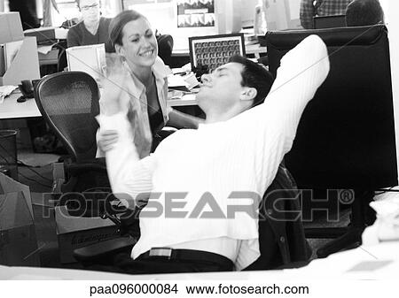 Picture - Woman and man in office, man stretching, woman smiling and holding man's arm, B&W. Fotosearch