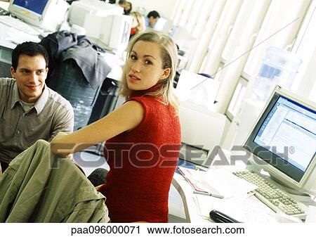 Stock Image - Woman sitting at desk, looking over shoulder at camera. Fotosearch