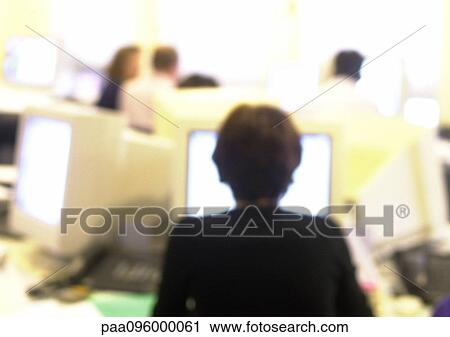 Stock Image - Woman working at computer in office, blurred, rear view. Fotosearch